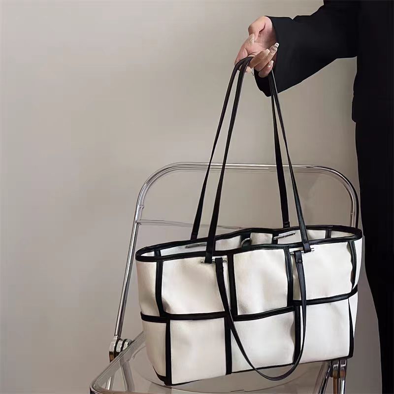 Side profile of a black canvas tote bag featuring a white grid pattern and long shoulder straps.