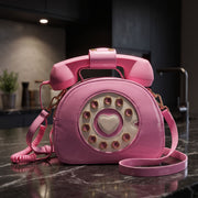 Retro telephone shaped crossbody bag with rotary dial and heart detail resting on a dark marble kitchen countertop.